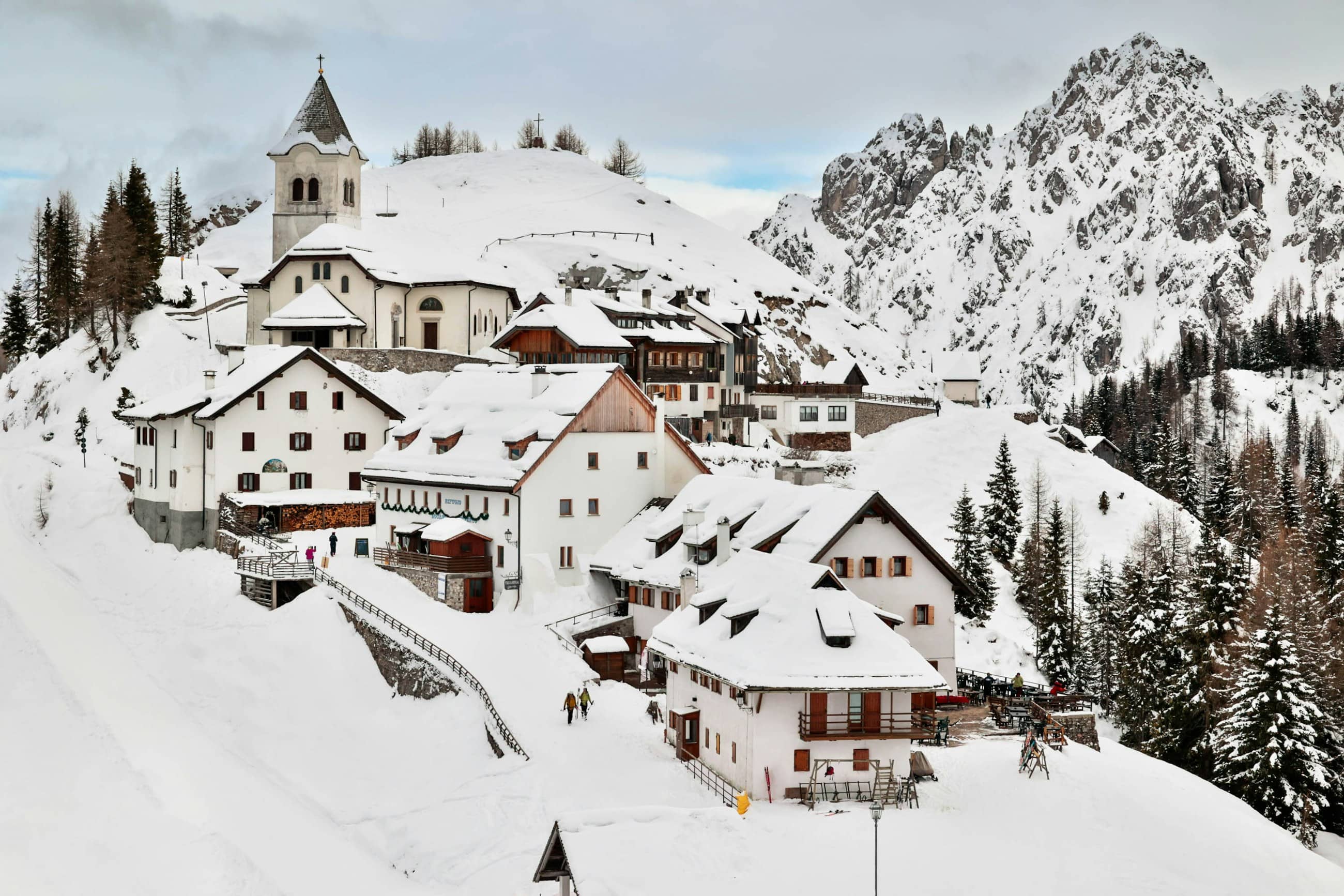 A mountain village under deep snow, a church tower above the roofs and bare rock behind.