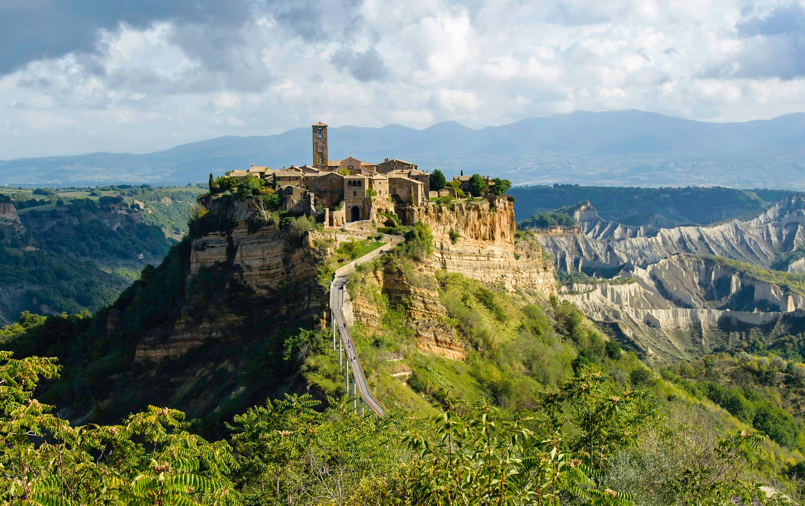 Civita di Bagnoregio on its tufa outcrop, eroded badlands dropping away on every side and a footbridge running out to it.
