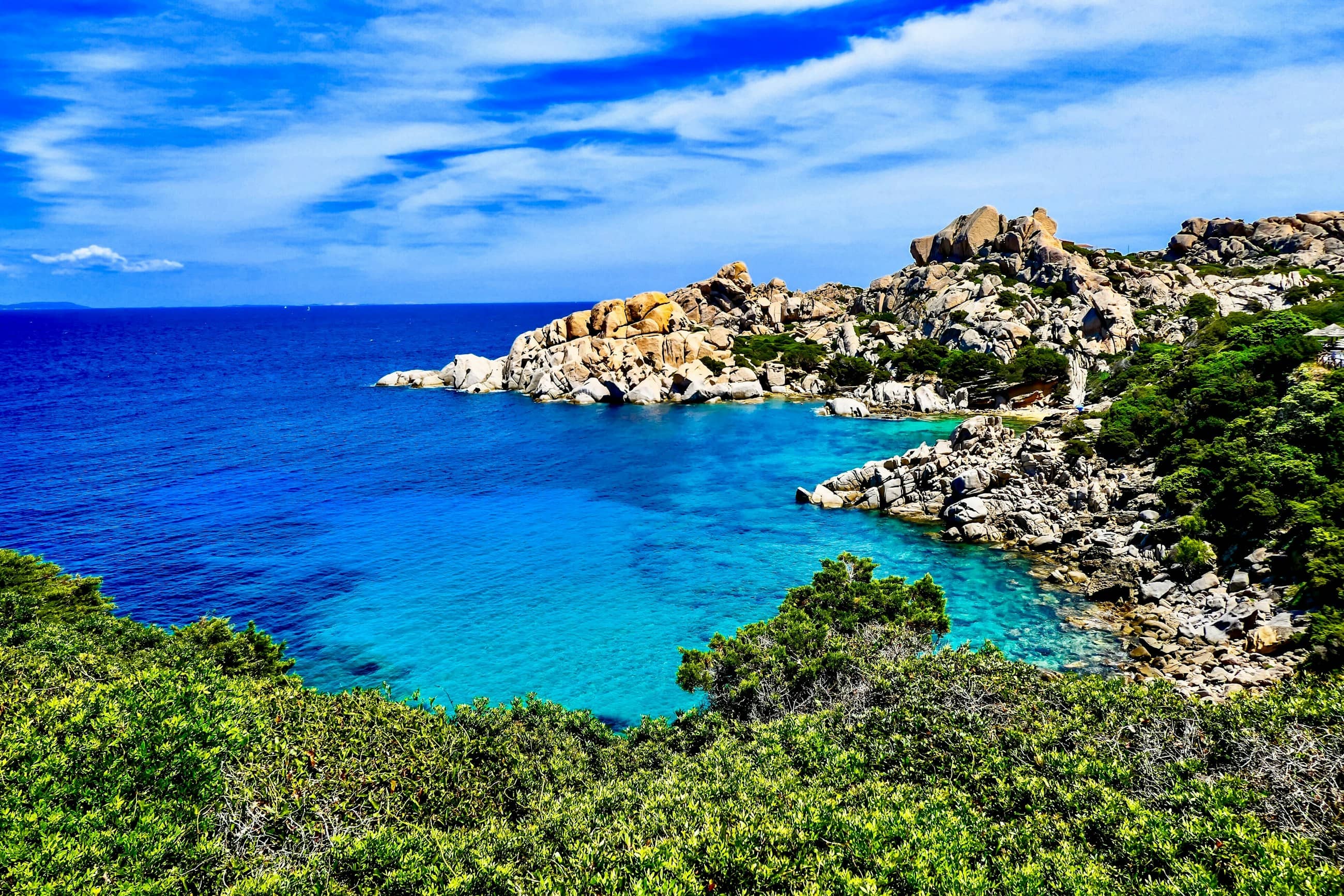 Granite boulders and low scrub above a clear turquoise inlet at Capo Testa.