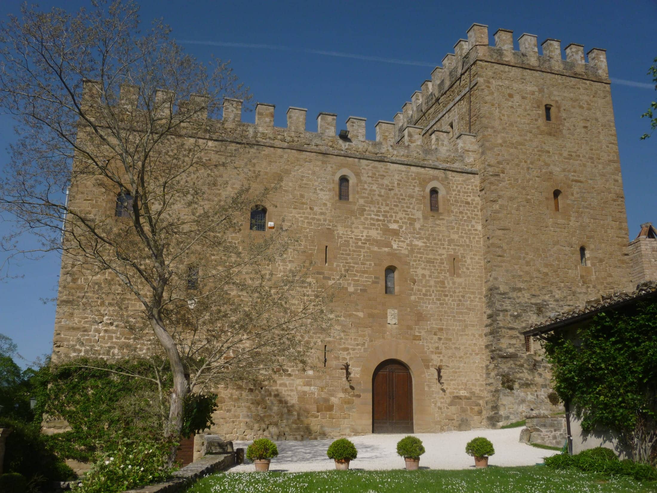 Castello di Rocca d'Ajello, Camerino, Marche: exterior: the castle's main front with the arched doorway, gravel apron, potted box and lawn, seen from the garden in full sun.