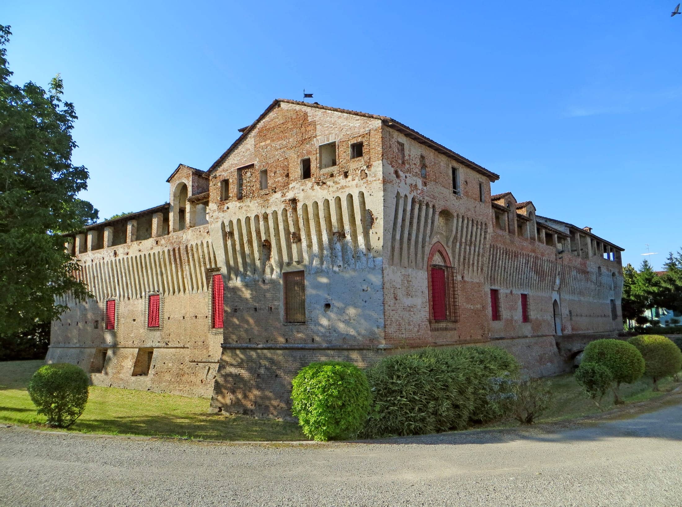 Castello di Roccabianca, Roccabianca, Emilia-Romagna: exterior: the south front and south-west flank of the whole castle, low sun, clipped hedges and gravel drive in frame, landscape orientation.