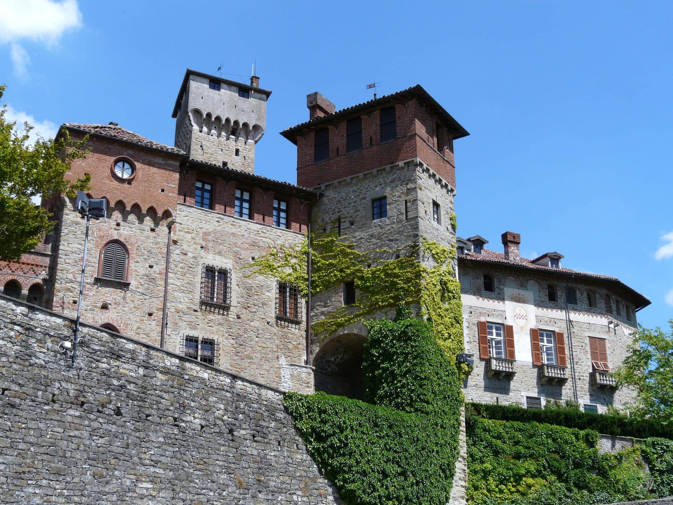 Castello di Tagliolo Monferrato, Tagliolo Monferrato, Piemonte: exterior: the tower, the brick loggia block and the shuttered residential wing above the boundary wall and ivy terrace, deep blue sky, landscape orien.