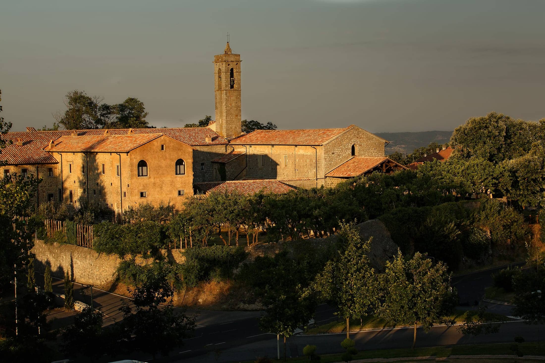 Convento San Bartolomeo, Piancastagnaio, Toscana: exterior: the whole convent range and its bell tower seen from across the road in low golden evening light, with the terrace and vines below.