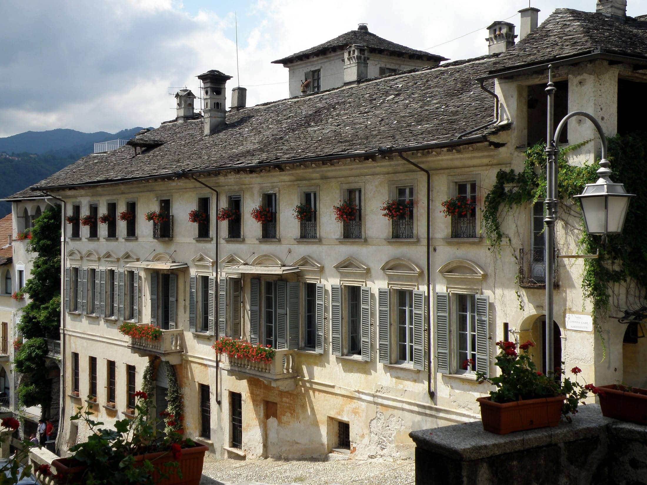 Palazzo Penotti Ubertini, Orta San Giulio, Piemonte: exterior, the full length of the palazzo facade with its stone-slab roof, shuttered windows and geranium balconies, seen from the sloping lane.