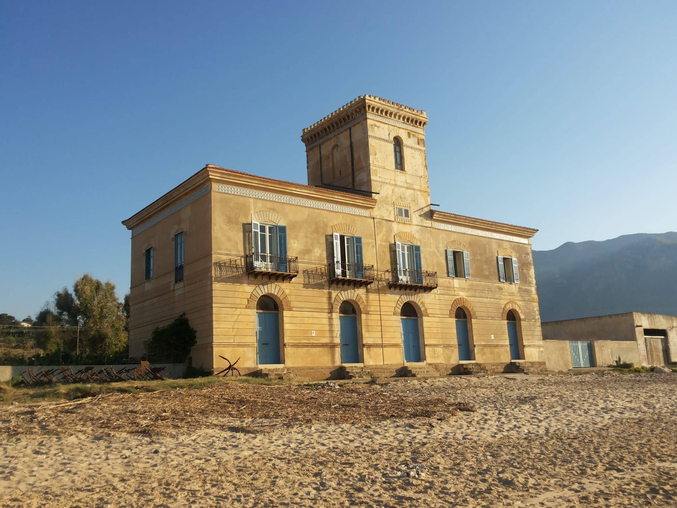 Tonnara Foderà di Magazzinazzi, Alcamo, Sicilia: exterior, three-quarter view of the main tonnara building from the beach in low golden light, mountain behind.
